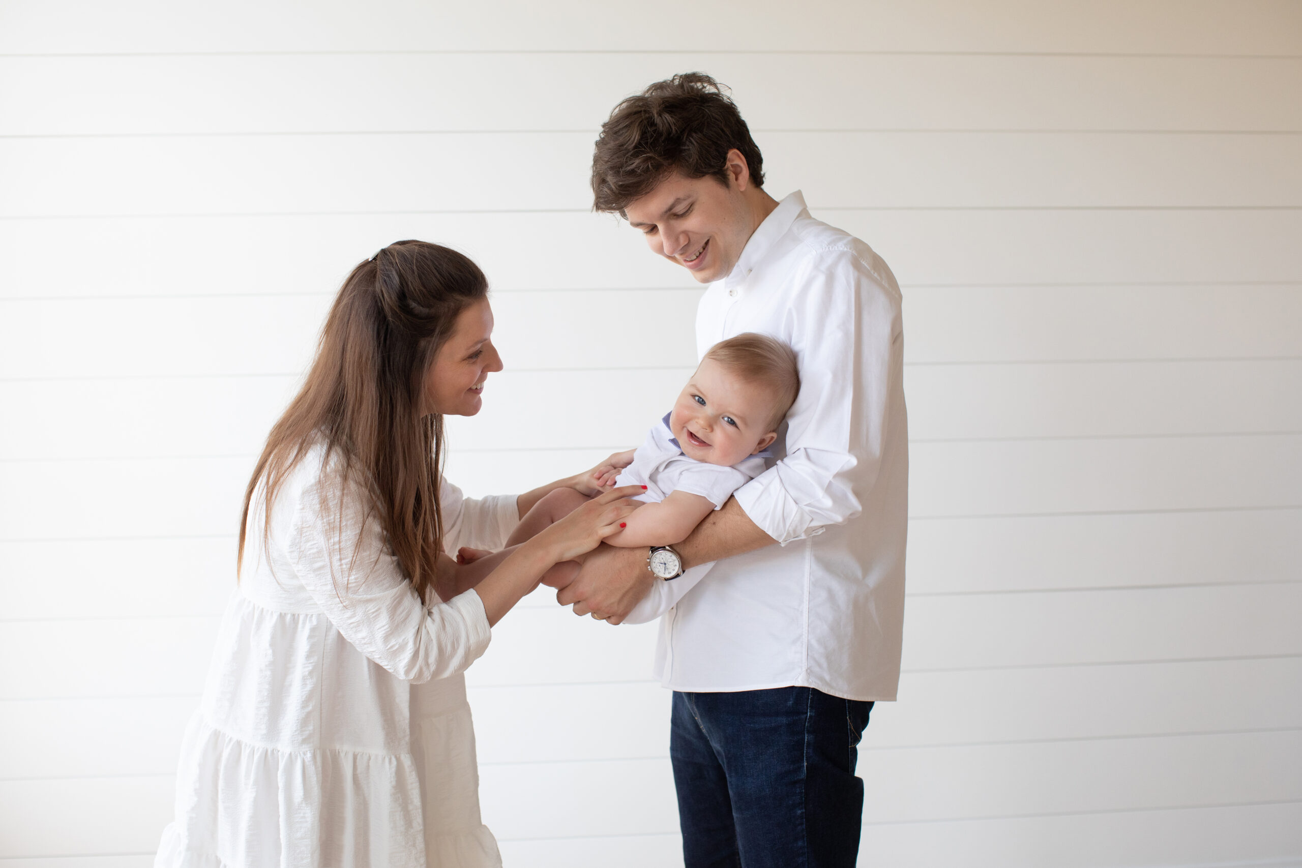 Mom and dad holding baby boy by the window for his six month session.