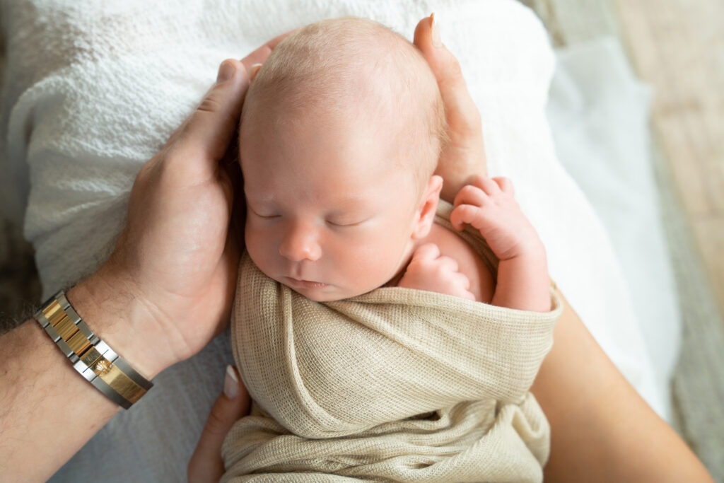 Mom & Dad's hands holding newborn baby.