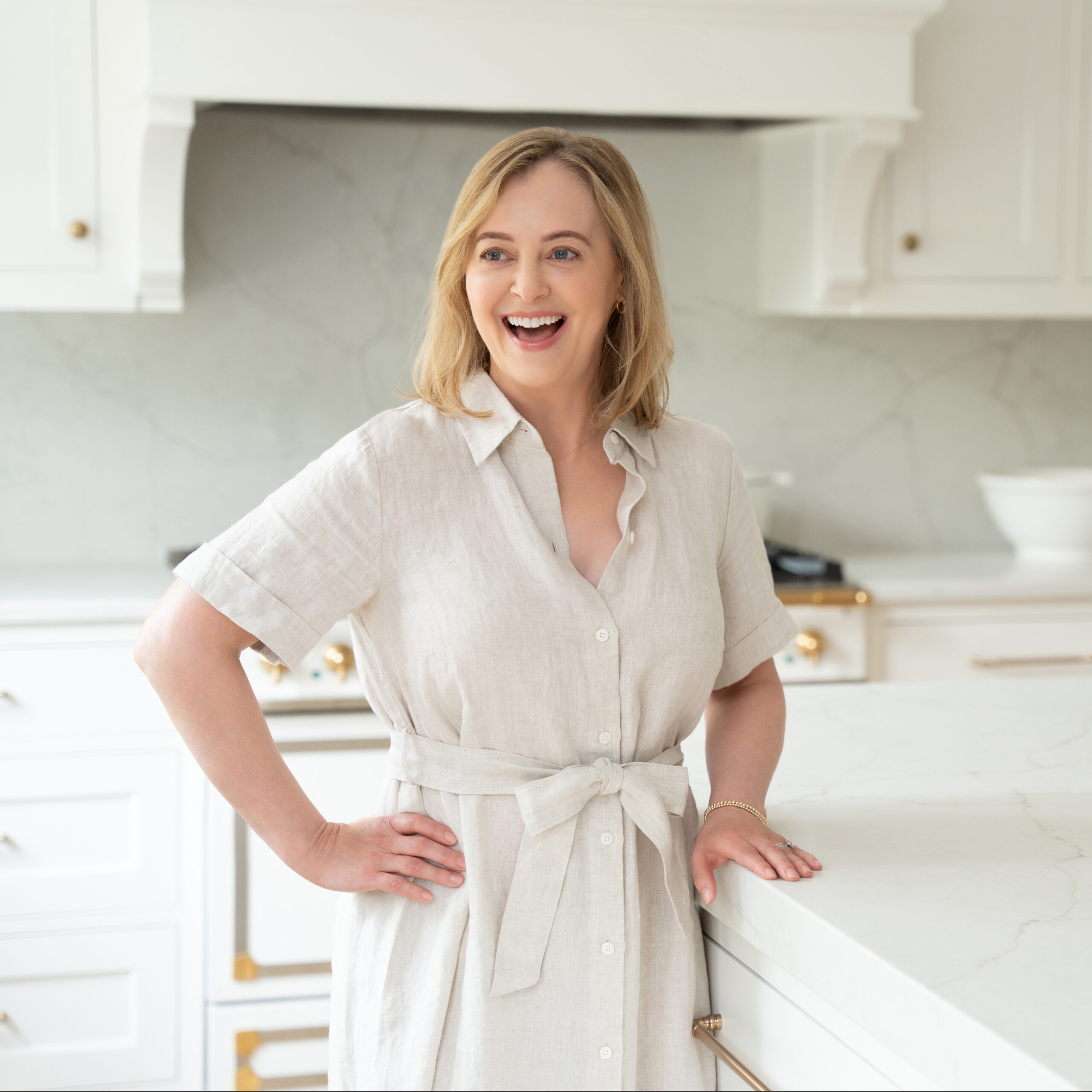 Woman in linen dress standing in kitchen laughing