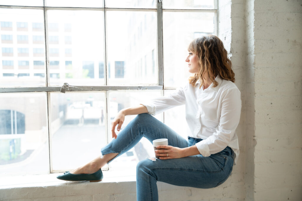 woman sitting in window sill looking out holding a coffee mug