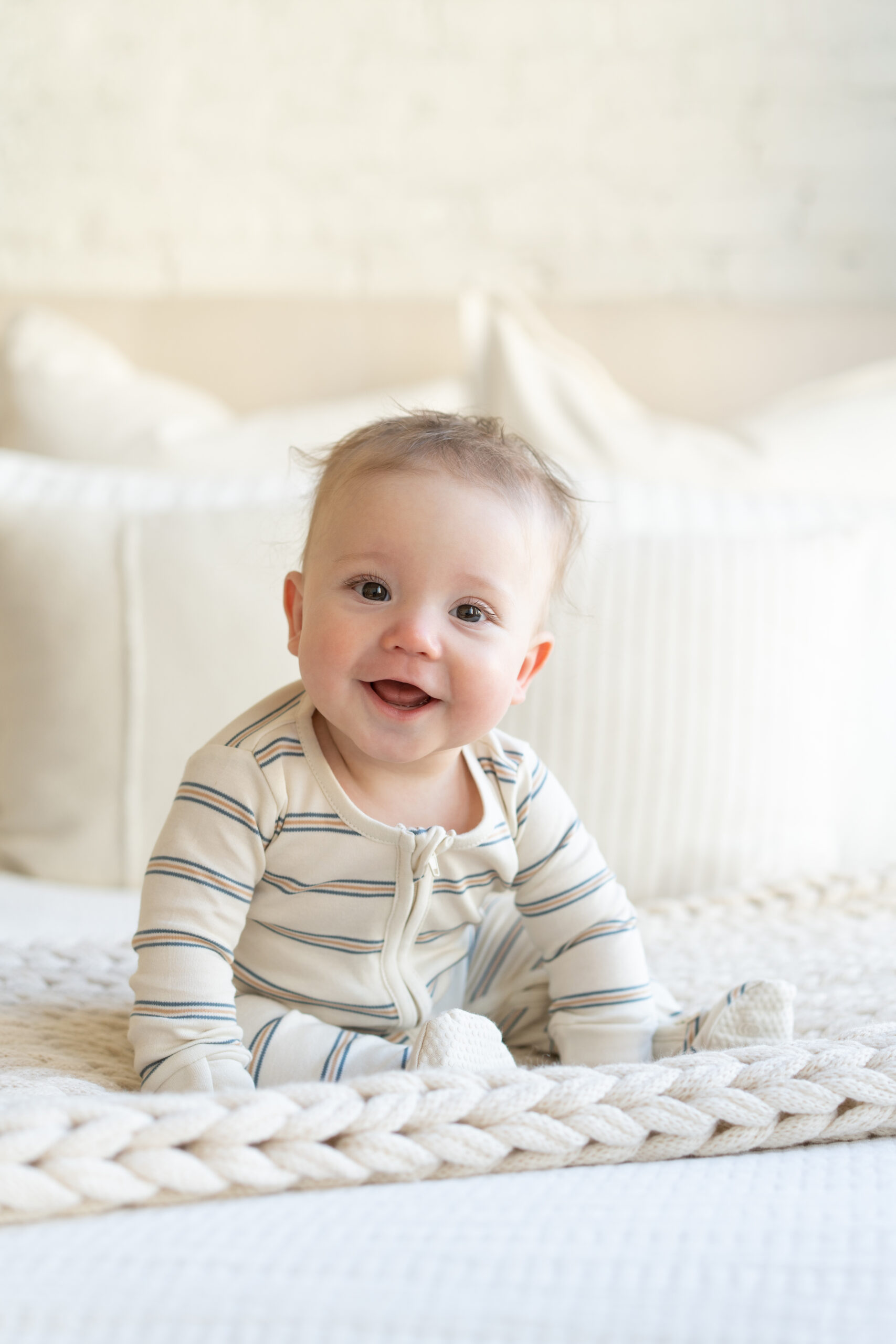 Six month old baby sitting on bed.
